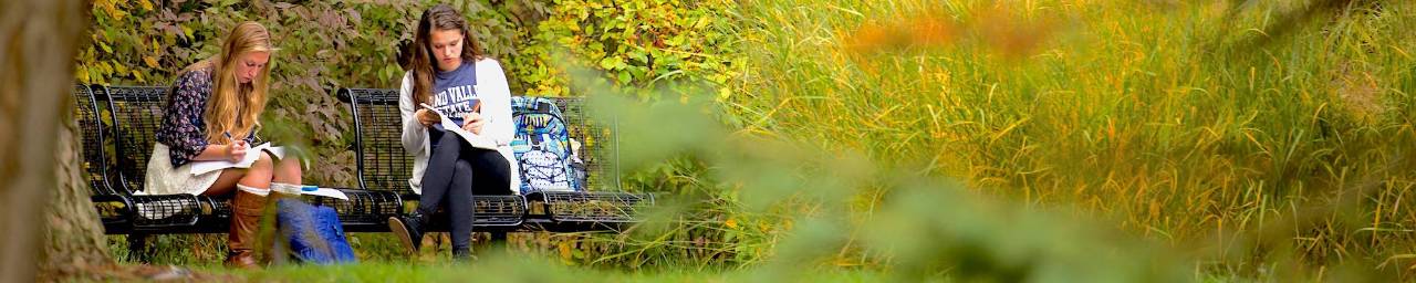 2 girls studying outside on a garden bench